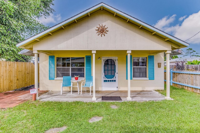 bungalow-style home featuring a front lawn, concrete block siding, and fence