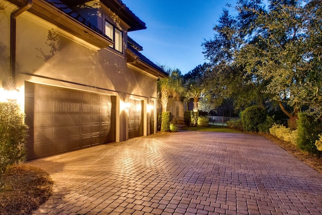 view of side of home featuring a garage, decorative driveway, and stucco siding