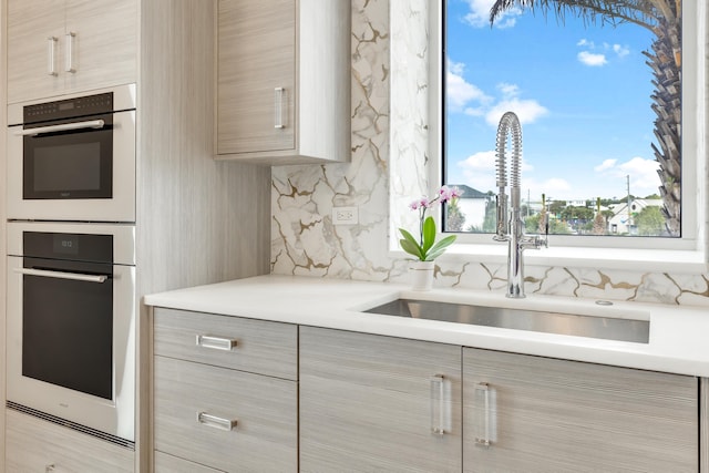 kitchen with light countertops, backsplash, light brown cabinets, a sink, and modern cabinets