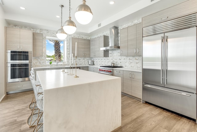 kitchen with light wood-style floors, wall chimney exhaust hood, a breakfast bar, and premium appliances