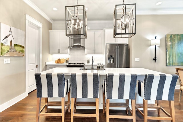 kitchen featuring high end fridge, a center island with sink, a sink, wall chimney exhaust hood, and a chandelier