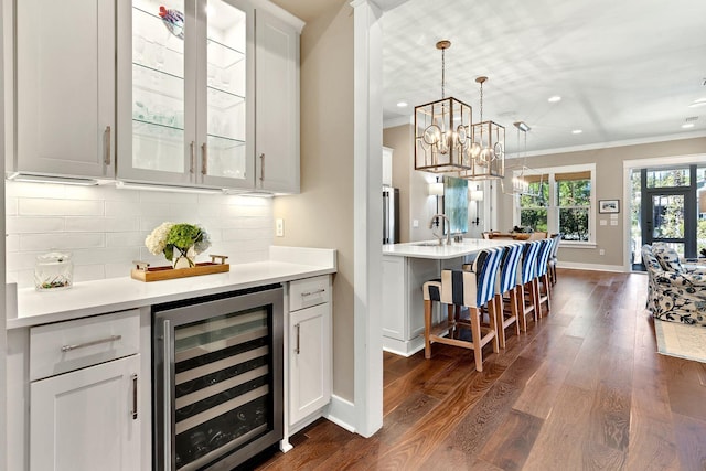 bar with tasteful backsplash, crown molding, beverage cooler, dark wood finished floors, and pendant lighting