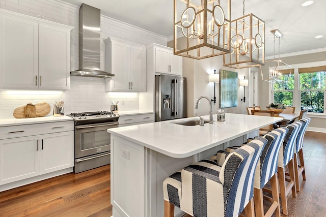 kitchen featuring wall chimney range hood, ornamental molding, a notable chandelier, stainless steel appliances, and a sink