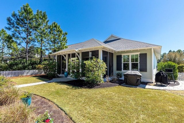 back of house featuring a yard, fence, a shingled roof, and a sunroom