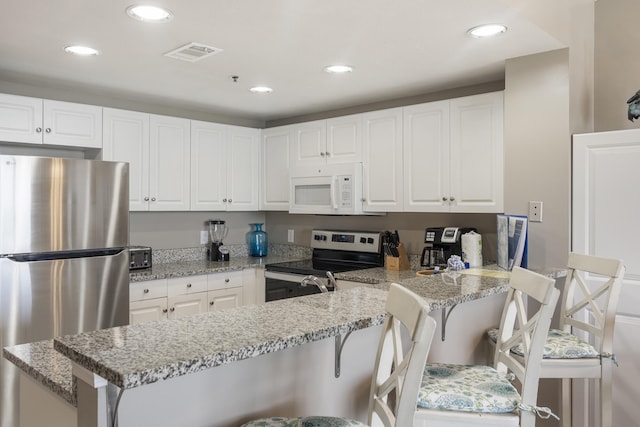 kitchen with a peninsula, appliances with stainless steel finishes, visible vents, and white cabinetry