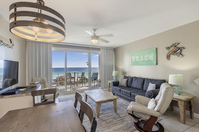 tiled living room with a tray ceiling, a water view, ceiling fan, and baseboards