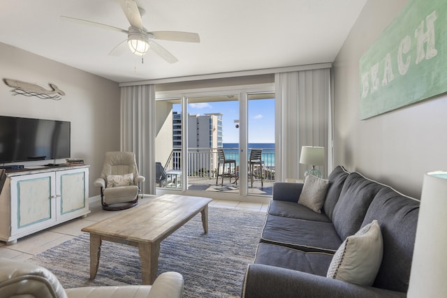 living area featuring light tile patterned flooring, a water view, a ceiling fan, and baseboards