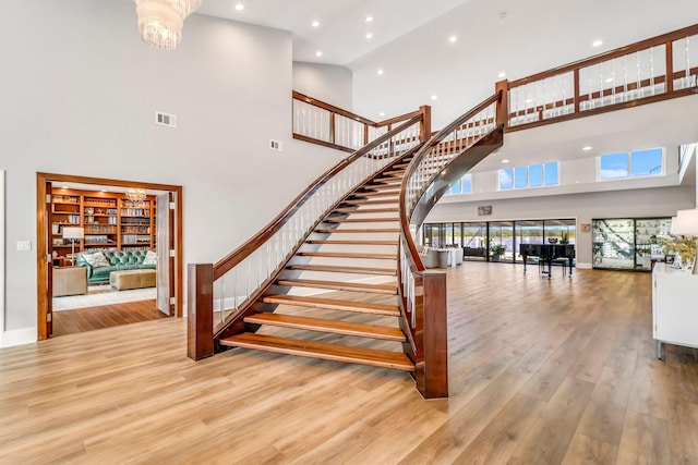 staircase with recessed lighting, visible vents, a towering ceiling, an inviting chandelier, and wood finished floors