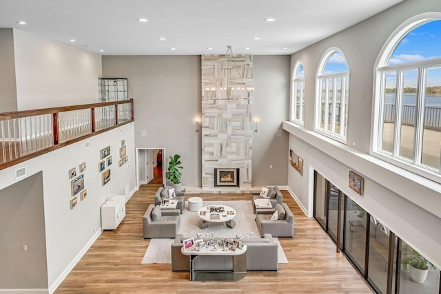 living area featuring visible vents, an inviting chandelier, light wood-style floors, a large fireplace, and baseboards