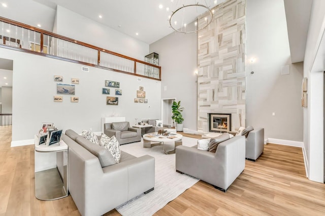 living room featuring light wood-type flooring, a high end fireplace, a towering ceiling, and a notable chandelier