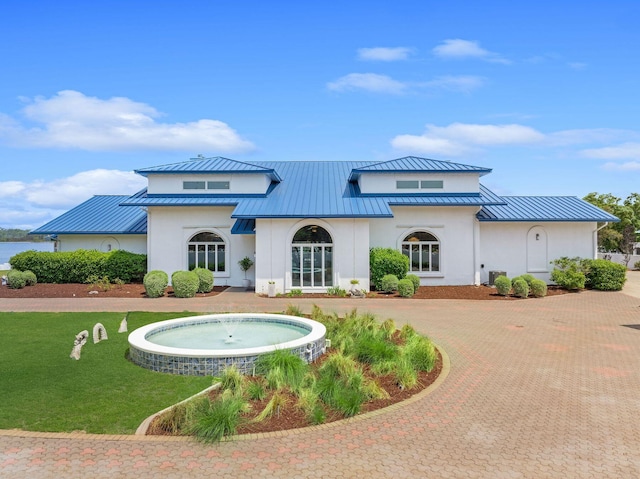 rear view of property with metal roof, decorative driveway, a standing seam roof, and a lawn