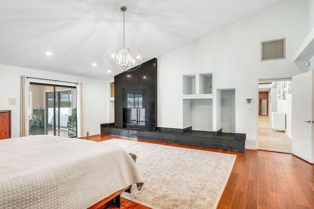 bedroom with high vaulted ceiling, a large fireplace, wood finished floors, visible vents, and access to exterior