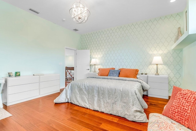 bedroom with wallpapered walls, a notable chandelier, visible vents, and wood finished floors