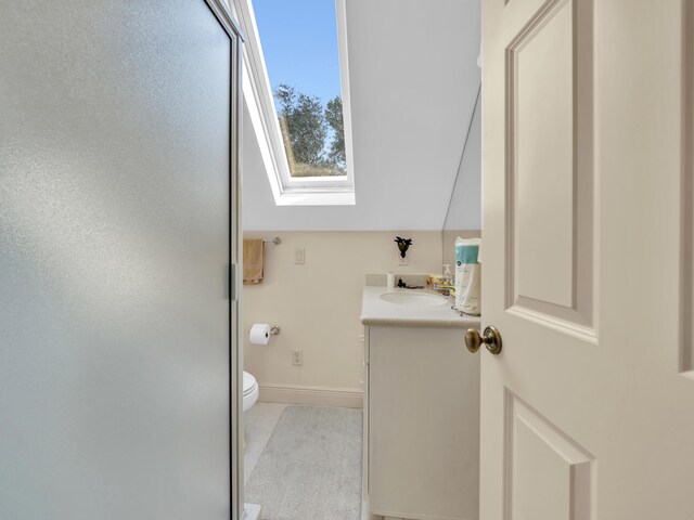 bathroom with toilet, a skylight, vanity, baseboards, and an enclosed shower