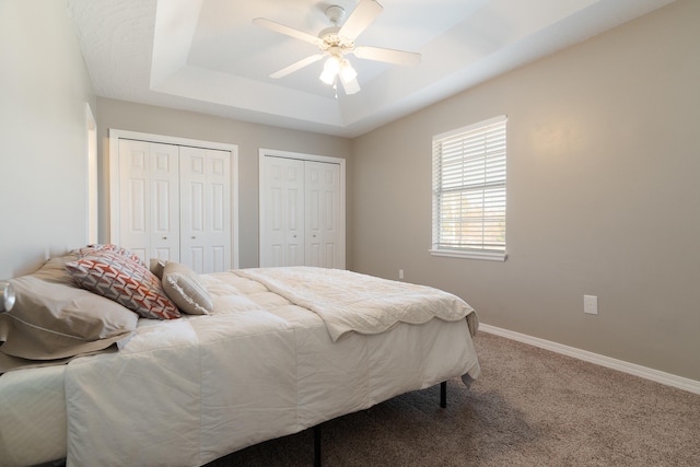 carpeted bedroom featuring baseboards, a raised ceiling, multiple closets, and a ceiling fan