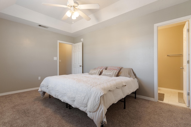 carpeted bedroom with visible vents, a raised ceiling, baseboards, and a ceiling fan