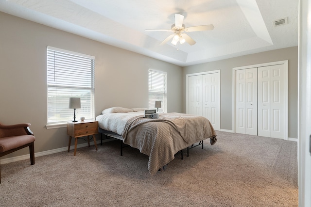 bedroom featuring visible vents, baseboards, a tray ceiling, light carpet, and two closets