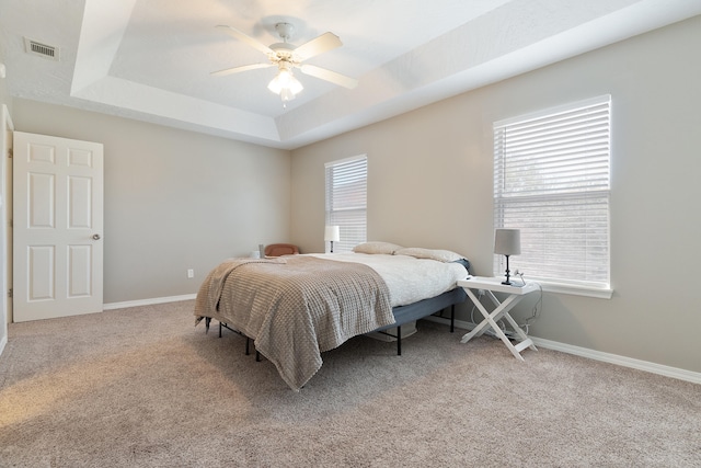 bedroom featuring visible vents, baseboards, a tray ceiling, ceiling fan, and light colored carpet