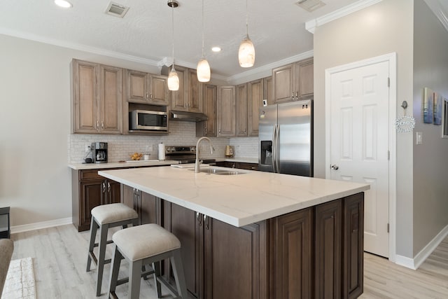 kitchen featuring visible vents, under cabinet range hood, a sink, backsplash, and appliances with stainless steel finishes