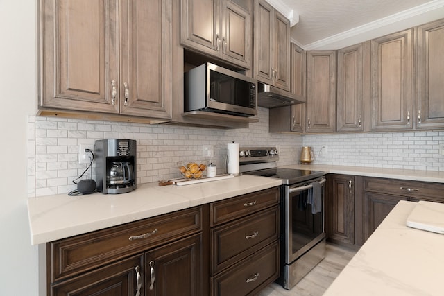 kitchen with backsplash, ornamental molding, under cabinet range hood, and stainless steel appliances