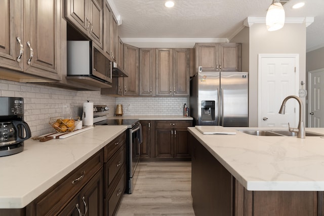 kitchen featuring light wood-style flooring, a sink, appliances with stainless steel finishes, crown molding, and tasteful backsplash