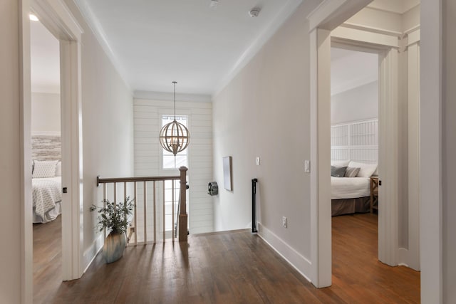 hall featuring crown molding, a notable chandelier, dark wood-type flooring, an upstairs landing, and baseboards