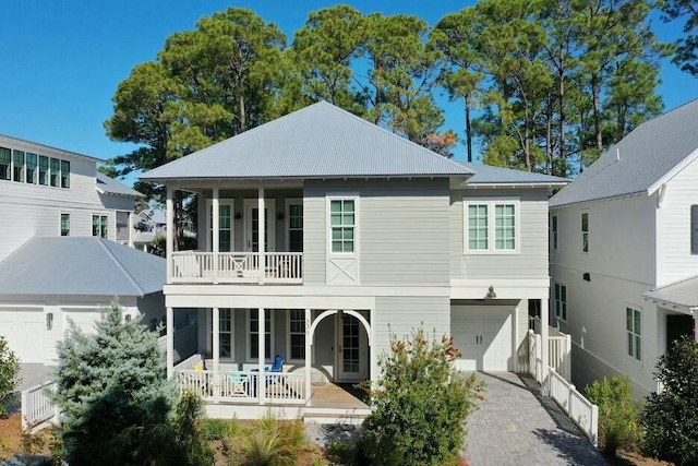 rear view of house featuring a balcony, an attached garage, a porch, and decorative driveway