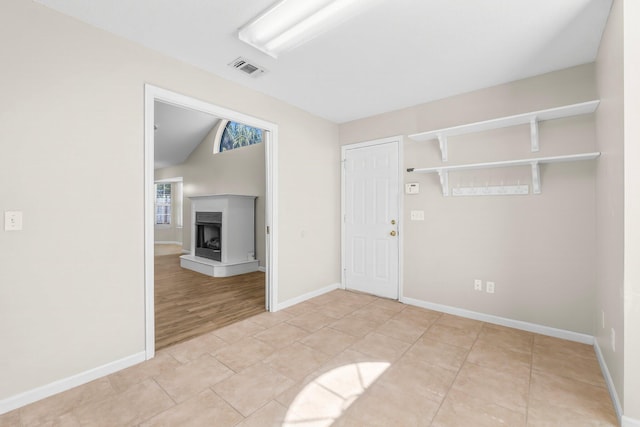 empty room with light tile patterned floors, baseboards, visible vents, and a fireplace with raised hearth