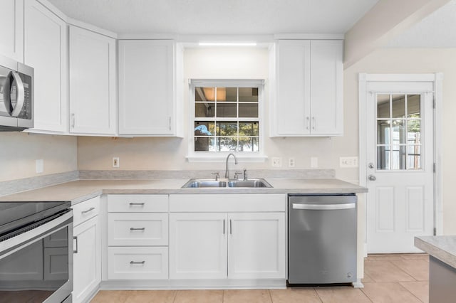 kitchen with light tile patterned floors, light countertops, appliances with stainless steel finishes, white cabinetry, and a sink