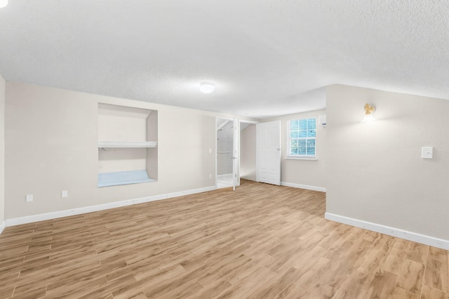 unfurnished room featuring light wood-type flooring, a textured ceiling, and baseboards