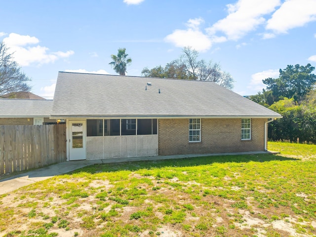 back of property featuring a shingled roof, fence, a lawn, and brick siding