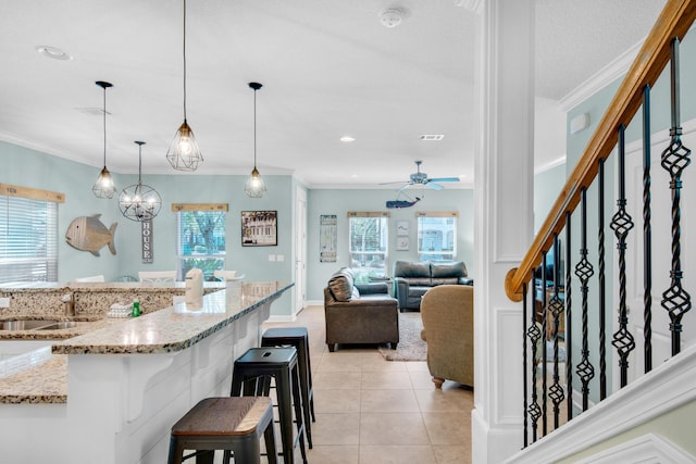 kitchen with decorative light fixtures, crown molding, light tile patterned floors, a sink, and a kitchen breakfast bar