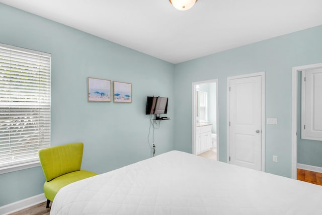 bedroom with ensuite bath, multiple windows, baseboards, and wood finished floors