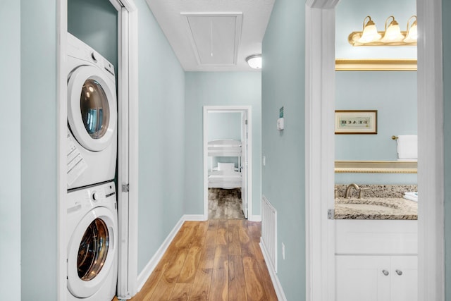 washroom with light wood finished floors, attic access, baseboards, stacked washer and clothes dryer, and a sink