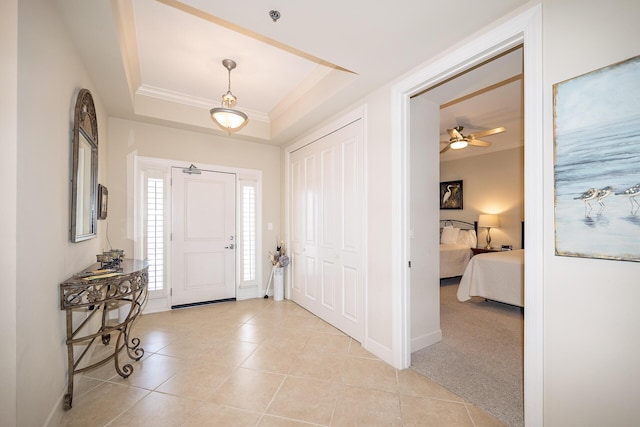 foyer entrance featuring a tray ceiling, ornamental molding, light tile patterned flooring, light carpet, and baseboards