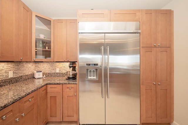 kitchen with built in refrigerator, stone countertops, glass insert cabinets, and decorative backsplash