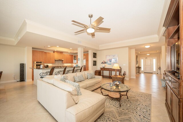 living area featuring light tile patterned floors, ceiling fan, baseboards, a tray ceiling, and crown molding