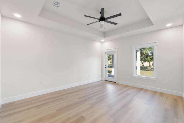 unfurnished room with a tray ceiling, light wood-style flooring, visible vents, and baseboards