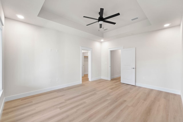 unfurnished bedroom with baseboards, a raised ceiling, a walk in closet, light wood-style floors, and recessed lighting