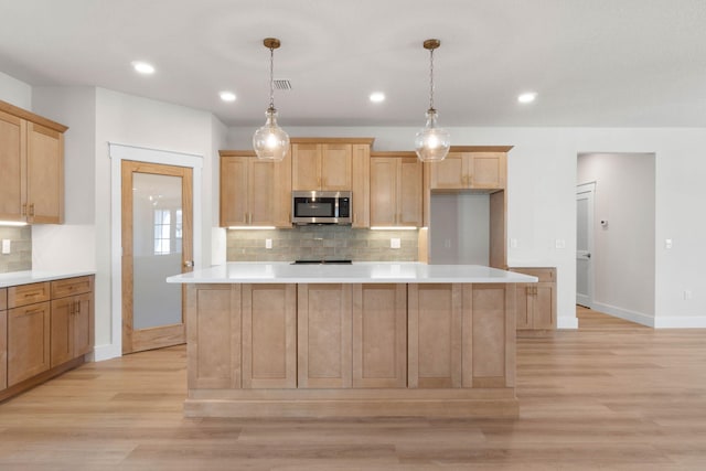 kitchen featuring light wood-style floors, light countertops, stainless steel microwave, and light brown cabinets