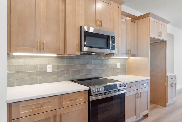 kitchen with stainless steel appliances, light countertops, decorative backsplash, light brown cabinetry, and light wood finished floors