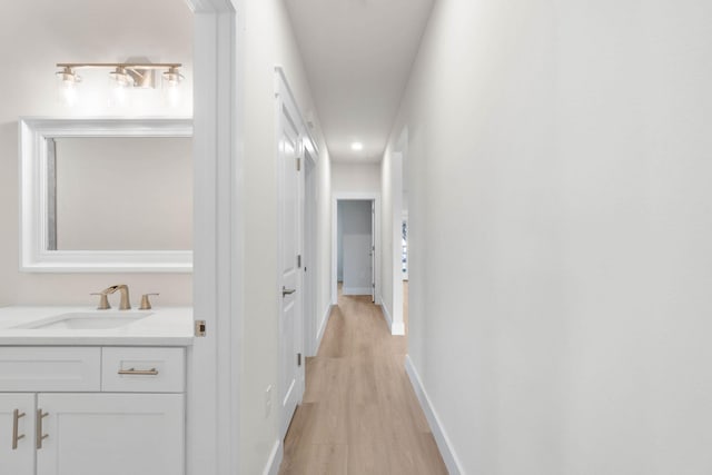 corridor featuring light wood-type flooring, a sink, and baseboards