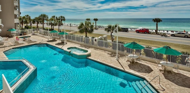 view of pool featuring a water view, a pool with connected hot tub, fence, and a patio