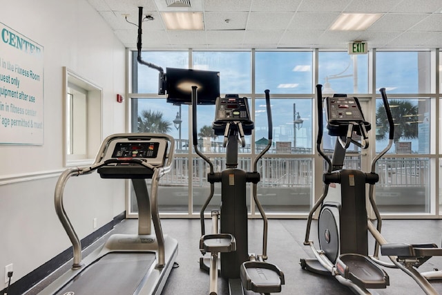 gym with a paneled ceiling, floor to ceiling windows, and baseboards