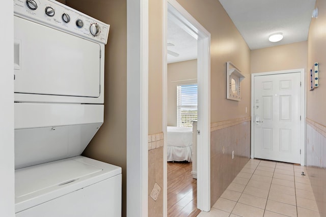 laundry area featuring a wainscoted wall, tile walls, stacked washer / dryer, light tile patterned flooring, and laundry area