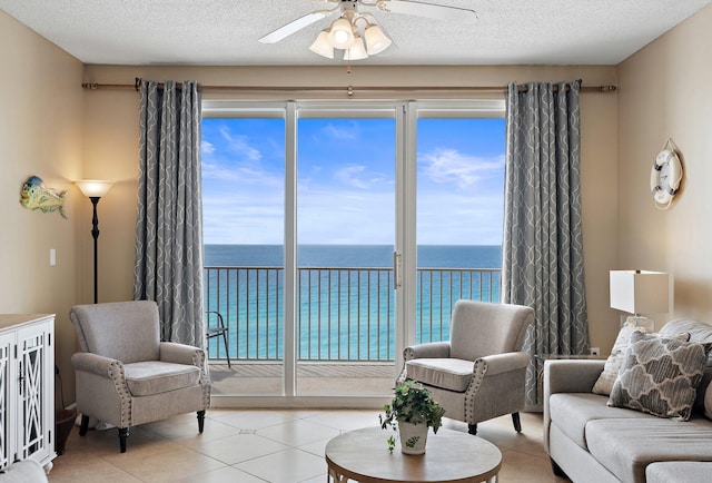 living room with a ceiling fan, a water view, plenty of natural light, and a textured ceiling