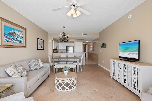 living room featuring ceiling fan with notable chandelier, visible vents, a textured ceiling, and light tile patterned floors