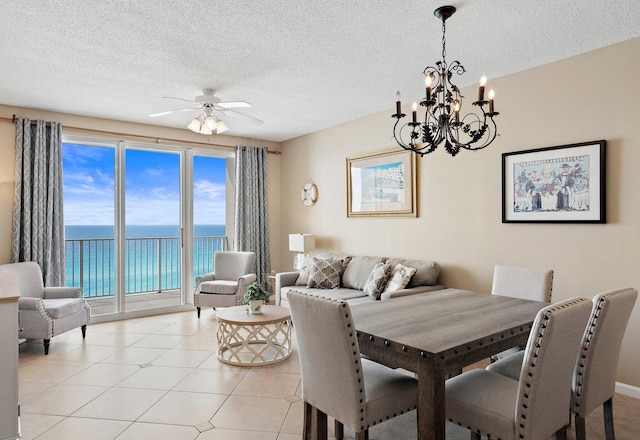 dining room with light tile patterned flooring, a water view, a textured ceiling, and ceiling fan with notable chandelier