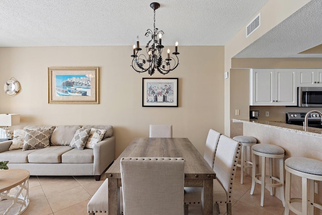 dining space featuring light tile patterned floors, a notable chandelier, visible vents, and a textured ceiling