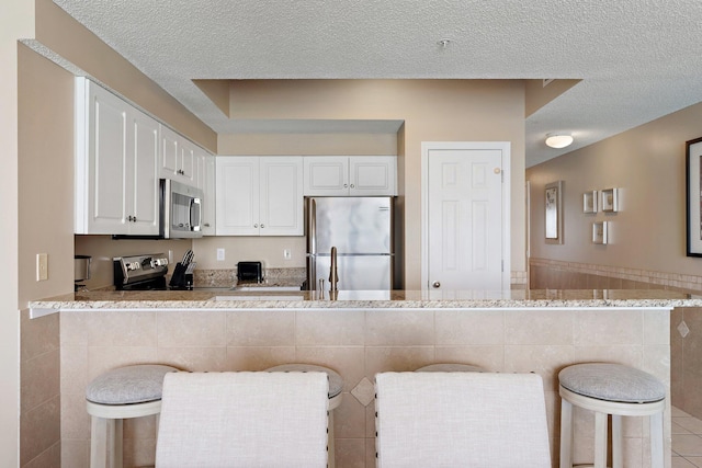 kitchen with stainless steel appliances, wainscoting, white cabinetry, and a textured ceiling